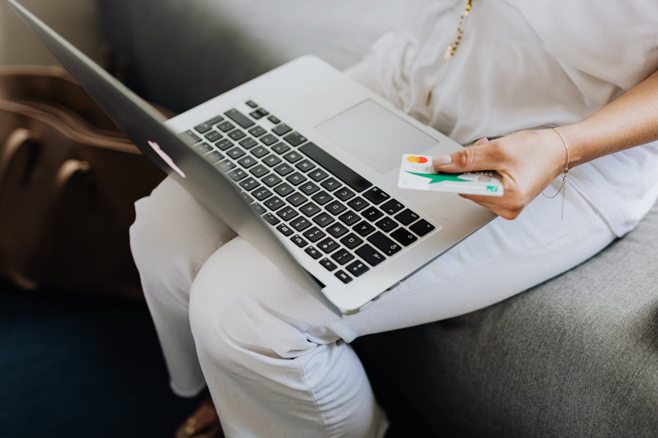 Adult using laptop and holding bank card for online shopping indoors.